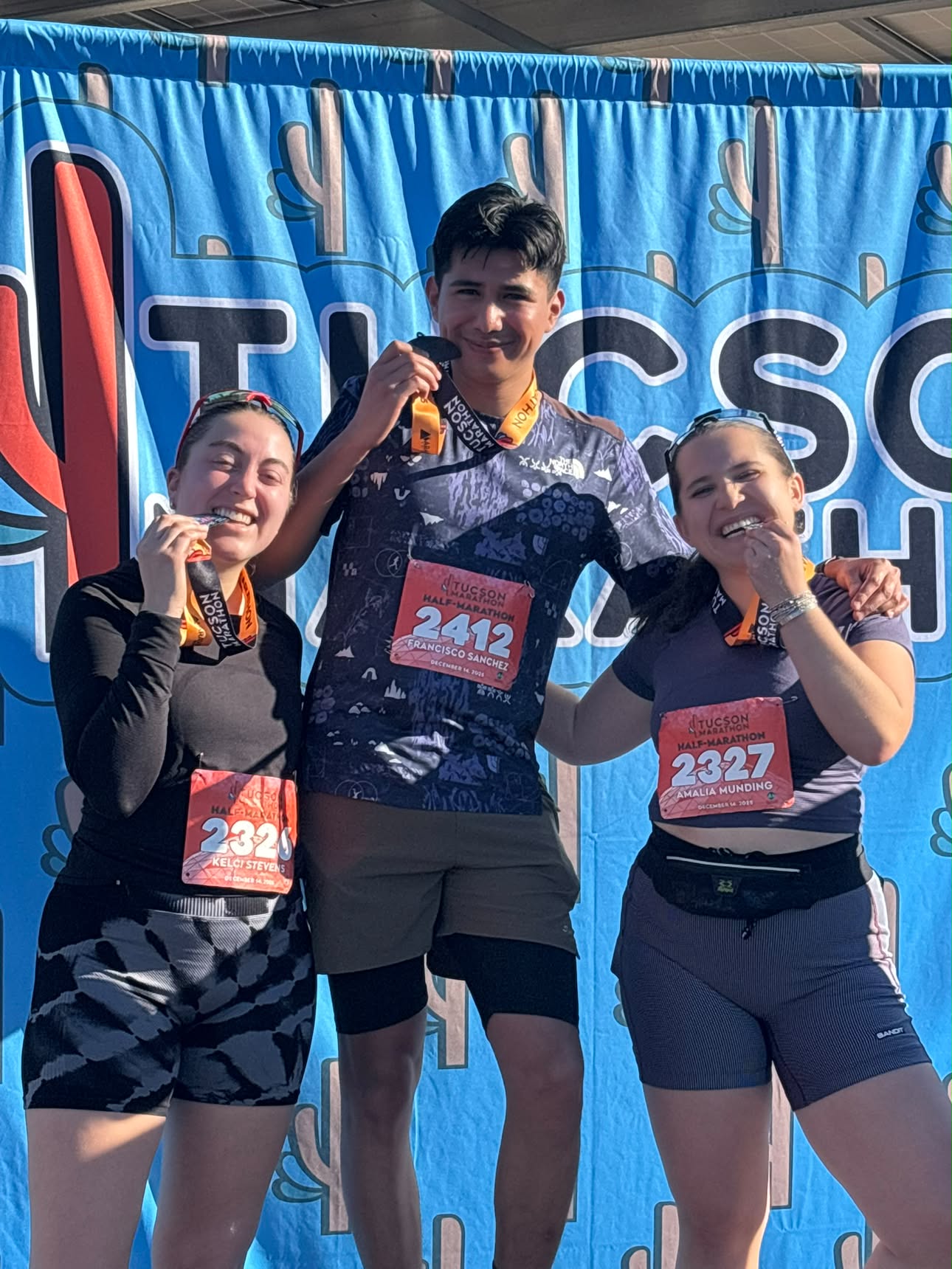 Three clients biting their medals after finishing the Tucson half marathon
